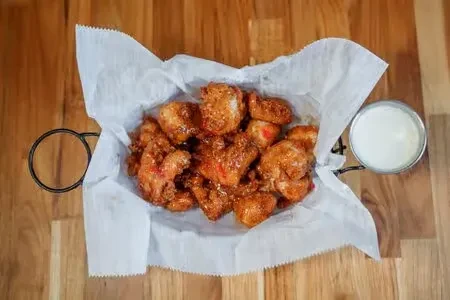 Basket of seasoned fried chicken with dipping sauce on a wooden table.