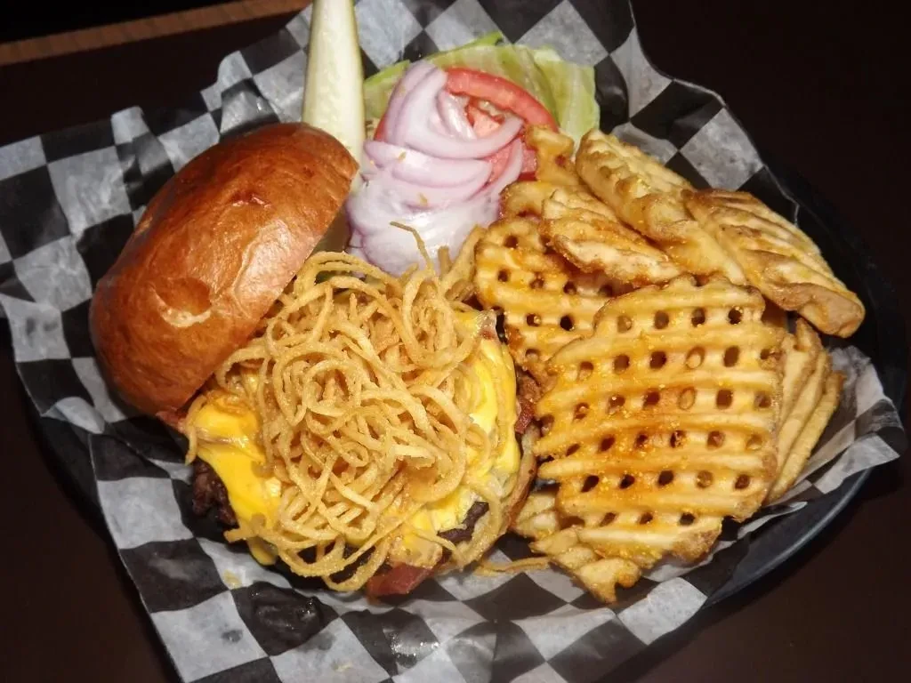 Cheeseburger with fried onions, waffle fries, and toppings served in a basket.
