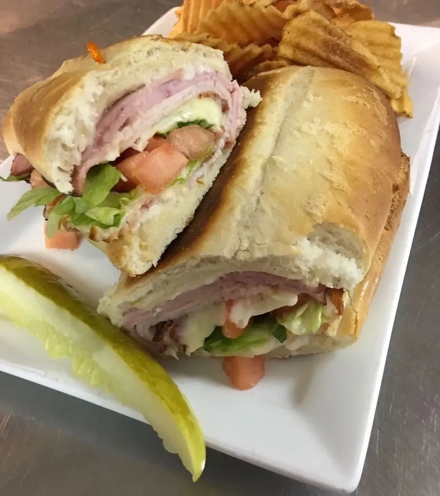 Loaded sub sandwich, waffle fries, and a dill pickle spear.