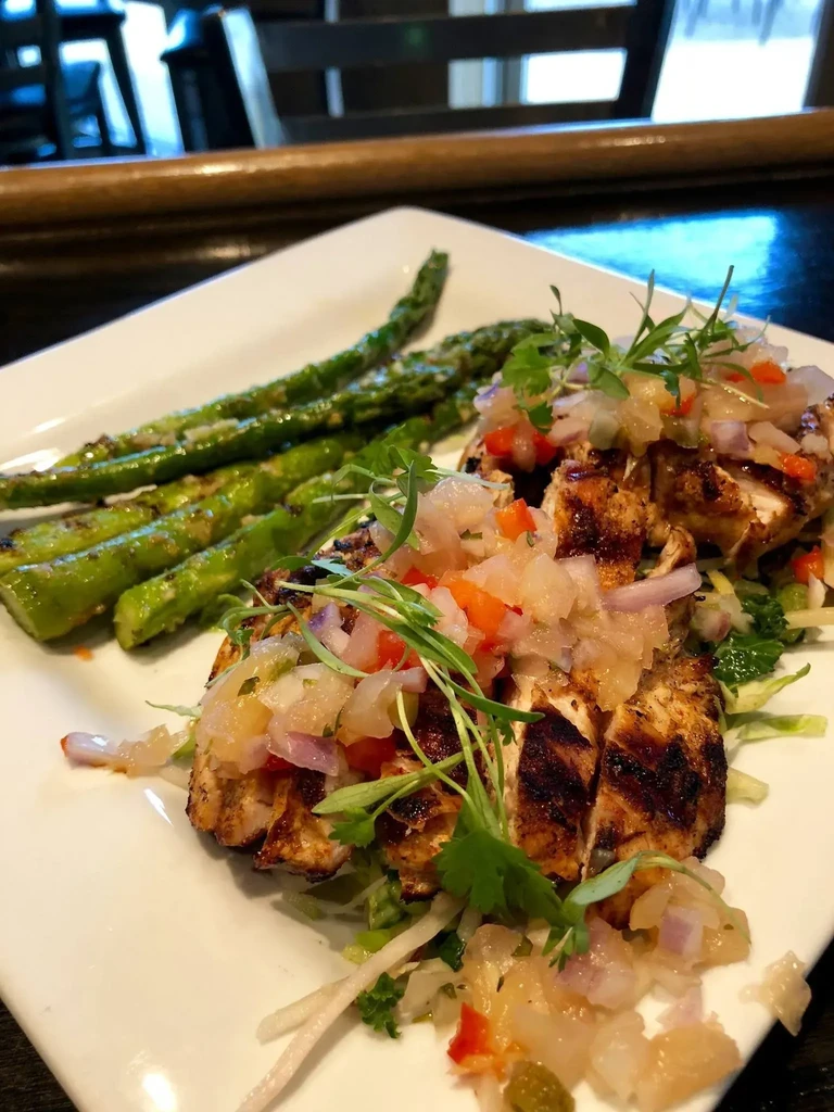 Plated grilled chicken topped with salsa, alongside asparagus.