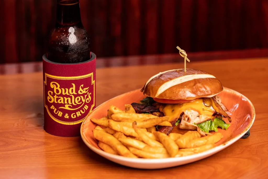 Pretzel bun burger, fries, and cold drink on a pub table.