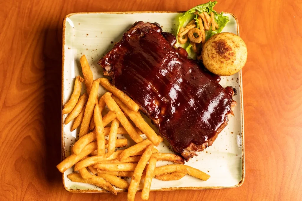 BBQ ribs, french fries, onion rings, lettuce, and a bun on a plate.