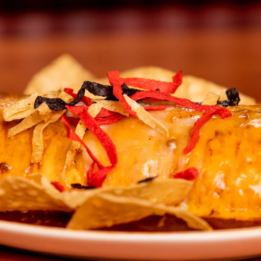 Close-up of a cheese-covered burrito with crispy strips and red sauce.