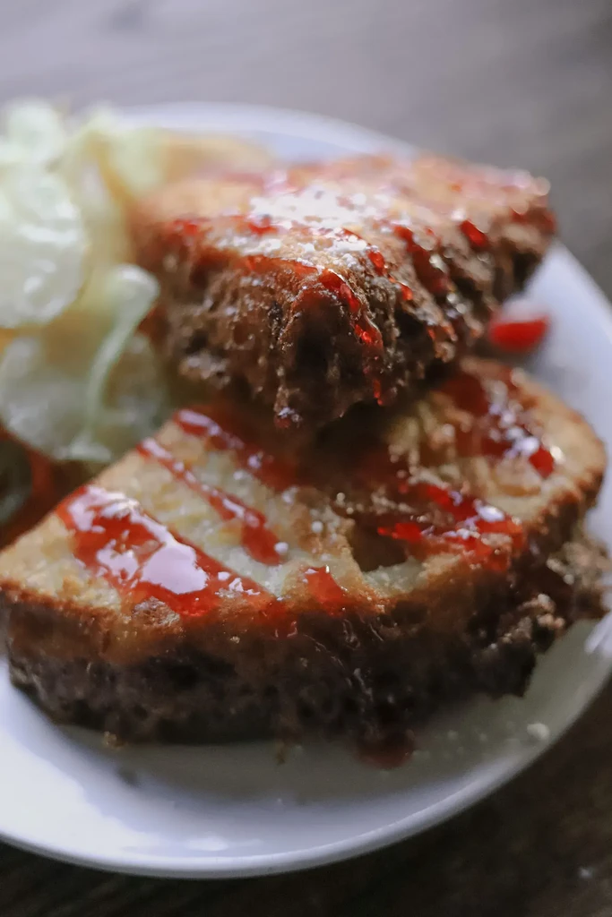 Close-up of golden-brown French toast with red sauce and powdered sugar.