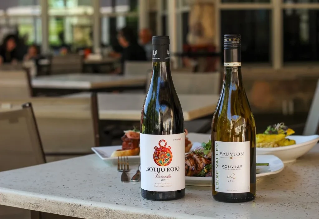 Two wine bottles, red and white, on an outdoor restaurant table.
