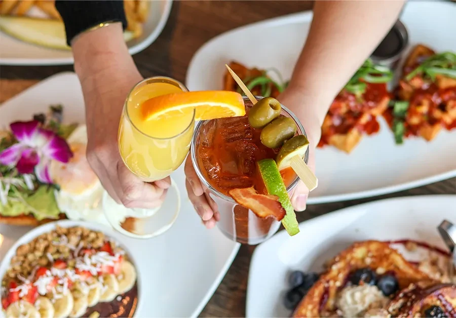 Two hands holding a mimosa and a Bloody Mary at brunch.