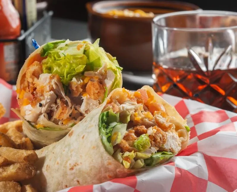 Grilled chicken wrap halves, fries, and drink on checkered paper.