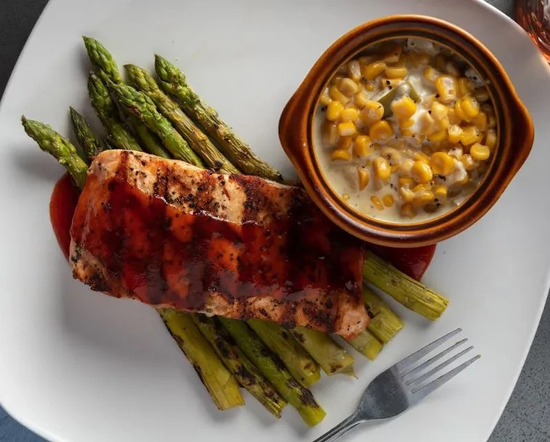 Grilled salmon, asparagus, and creamed corn on a white plate.