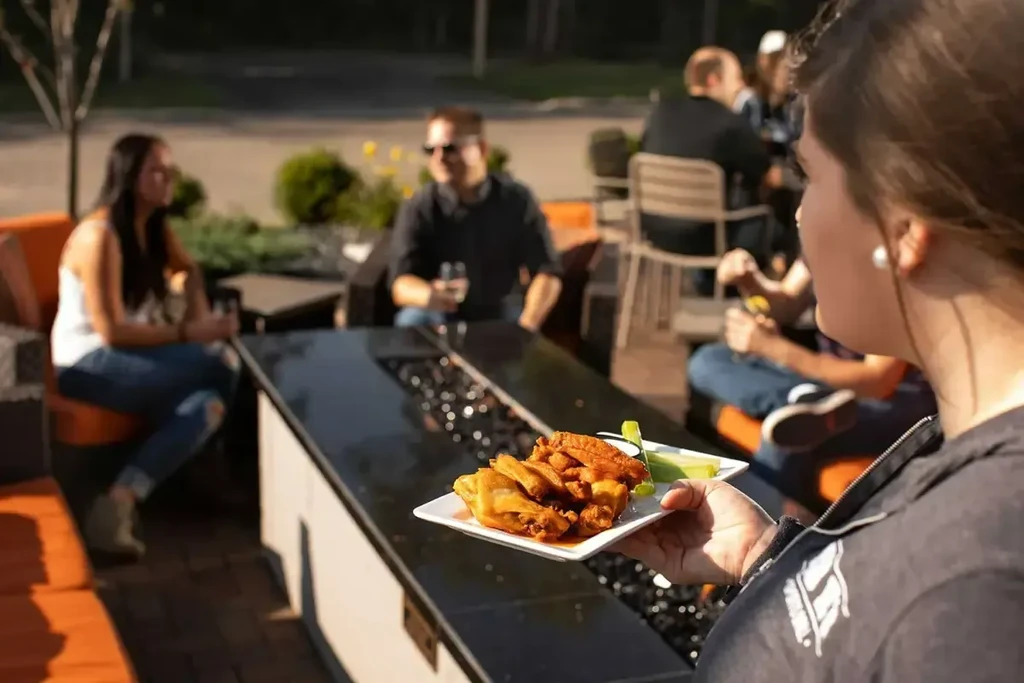 Server holds buffalo wings, celery, and dip on a sunny patio.
