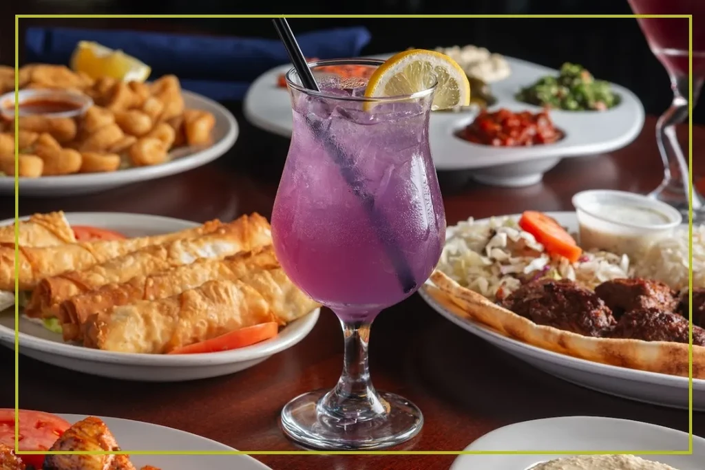 Ice-cold purple drink with lemon and straw, surrounded by appetizers.