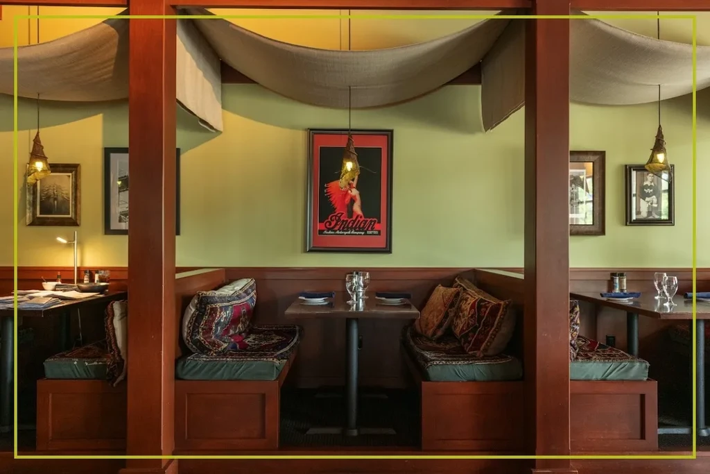 Cozy restaurant booths, olive walls, beige drapes, Indian poster above.
