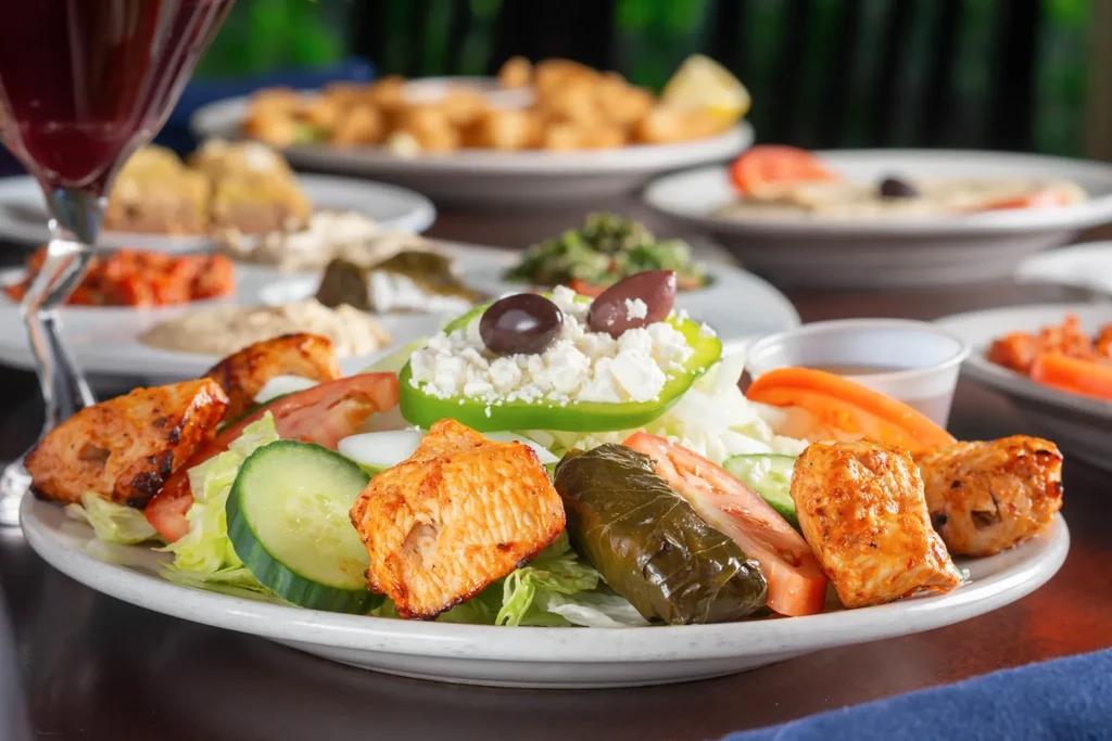Plate of Greek salad with grilled chicken, dolma, and blurred dishes.