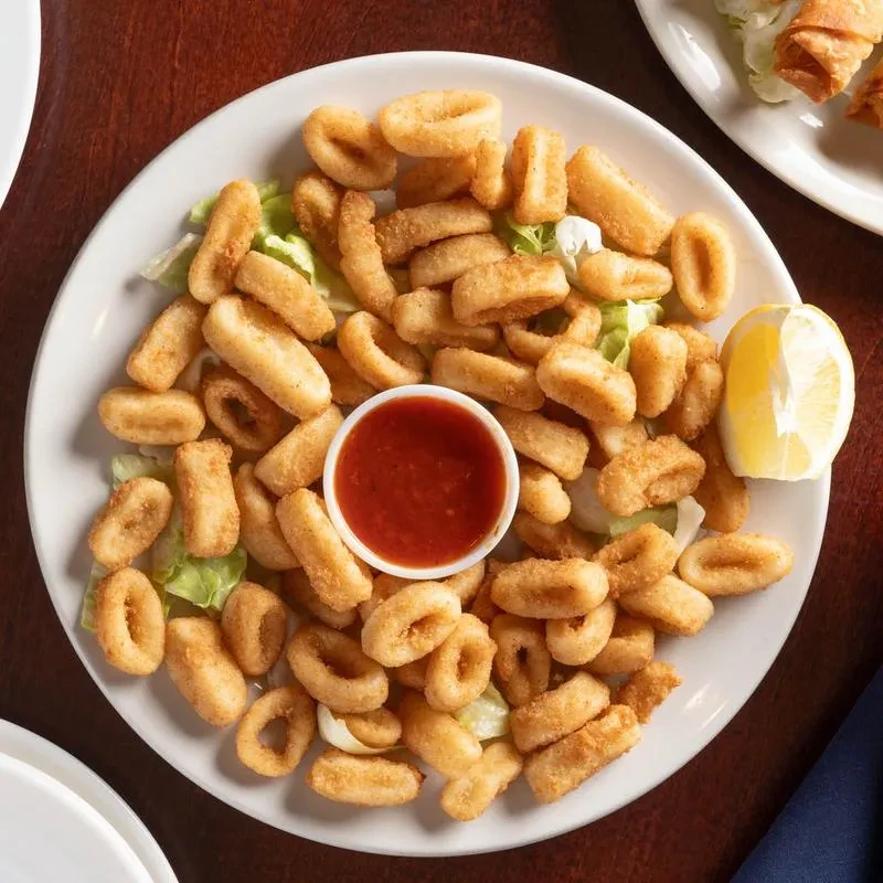 Fried calamari with red dipping sauce and lemon on a white plate.