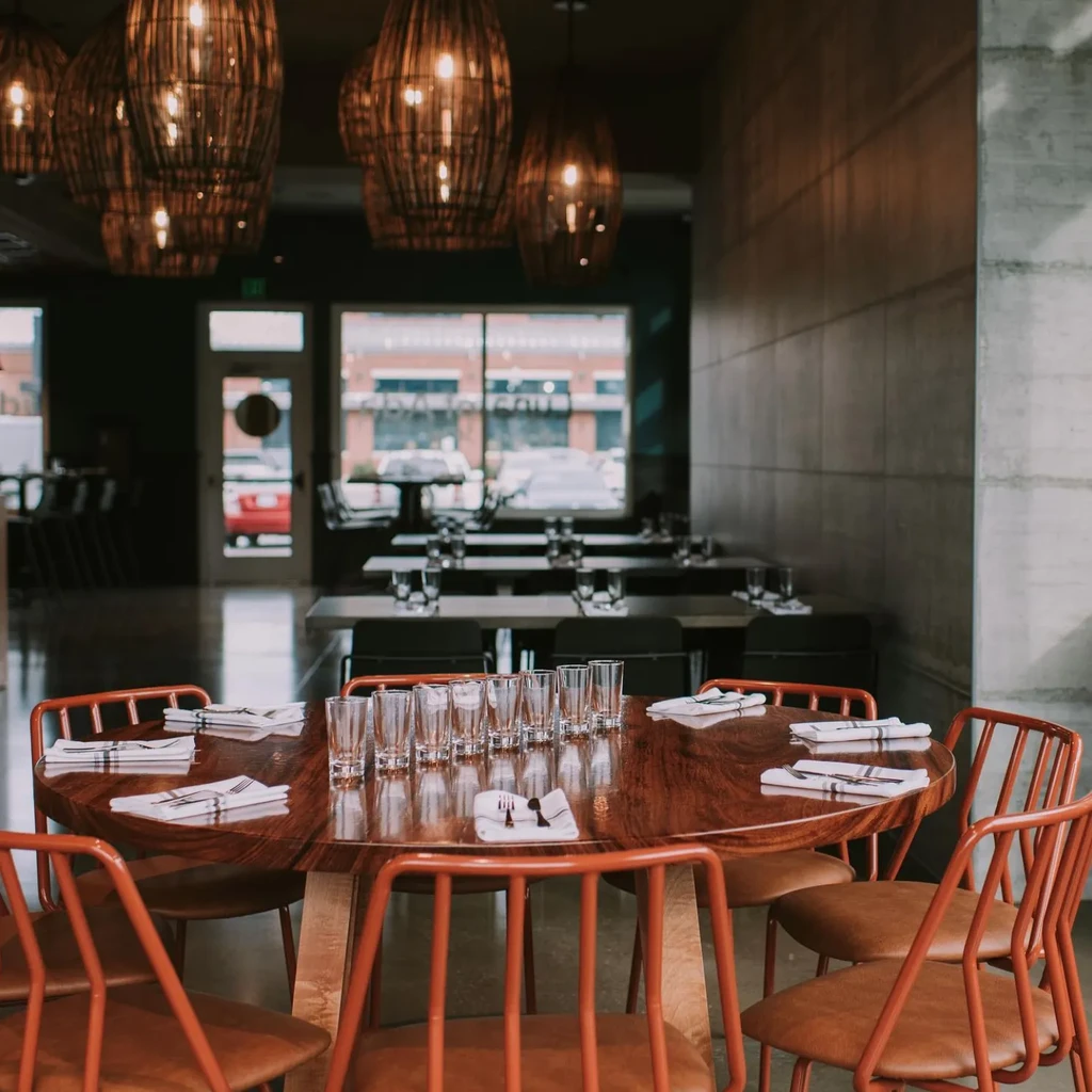 Restaurant interior with modern wooden table, reddish chairs, and wicker lights.