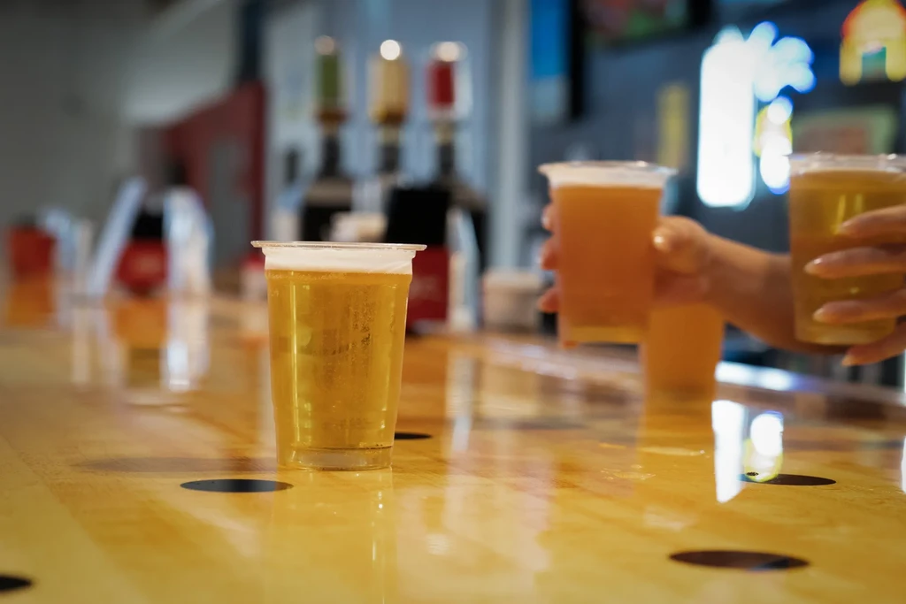Three plastic beer cups held by hands on a reflective bar.