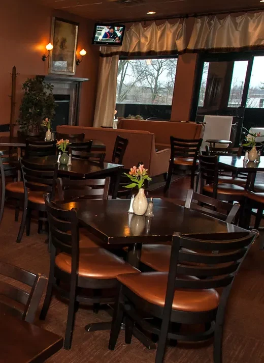 A warm, empty restaurant dining area with tables, fireplace, and window.
