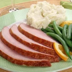 Slices of roasted ham, mashed potatoes, green beans, and orange garnish.