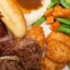 Plate with roast beef, mashed potatoes, gravy, vegetables, and potato patties.