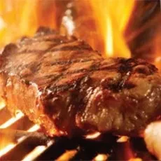 Close-up of a seared steak on a grill with flames.