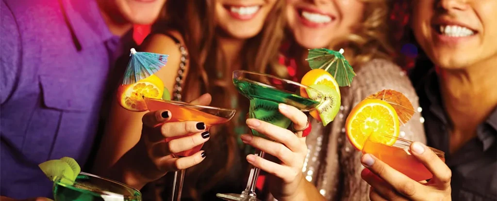 Colorful cocktails with fruit and umbrellas, held by smiling people.