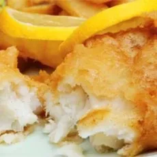 Broken open, flaky battered fish and chips, with a lemon wedge.