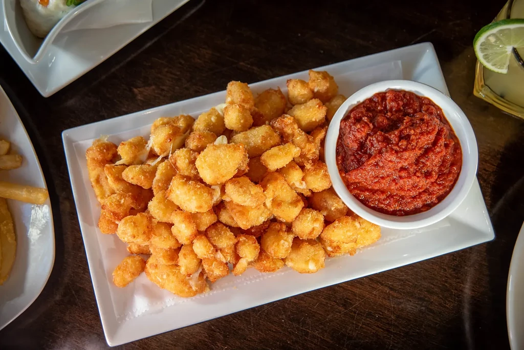 Golden-brown fried snacks with red dipping sauce on a white platter.