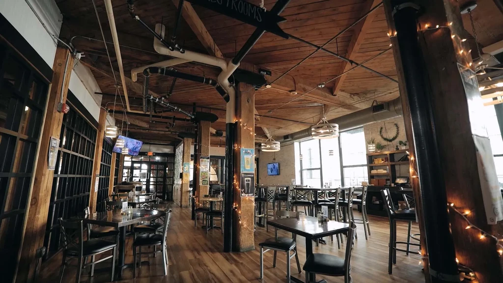 Empty industrial-chic restaurant with wooden beams, tables, and large windows.