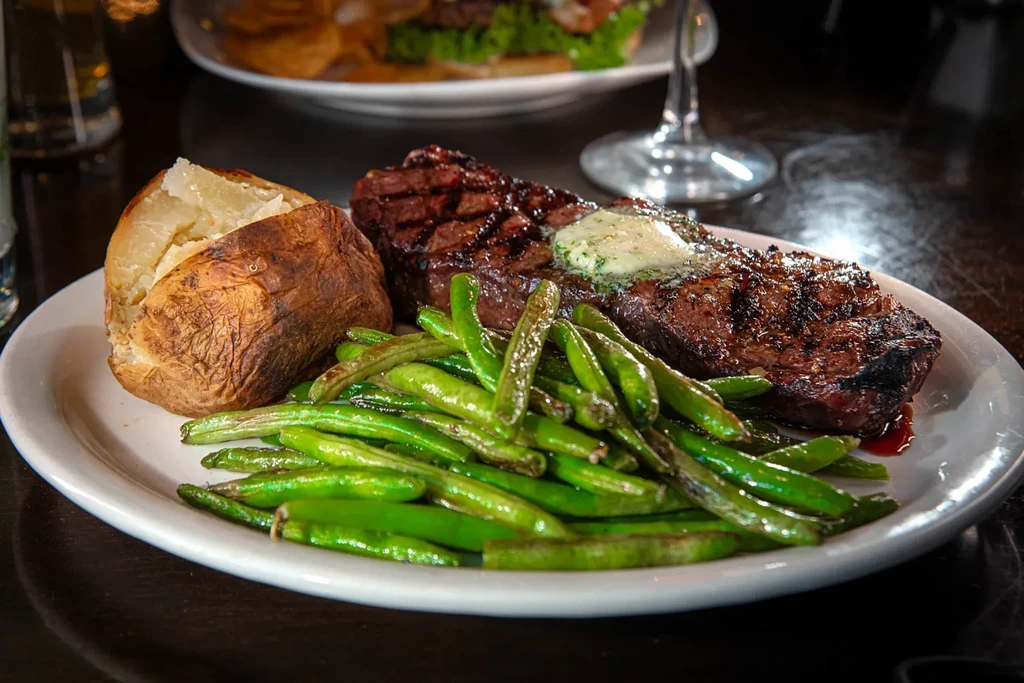 Grilled steak with melting butter, baked potato, and green beans.