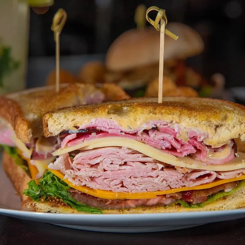 Hearty layered sandwich, cut in half, showcasing meat, cheese, and lettuce.