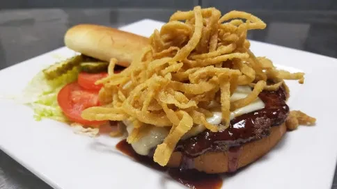 Open-faced burger with melted cheese, BBQ, crispy onion strings, and vegetables.