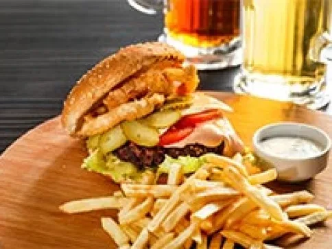 Burger, fries, and sauce on a wooden board with drinks.