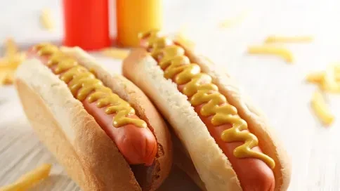 Two hot dogs with mustard, fries, and condiments on wood.
