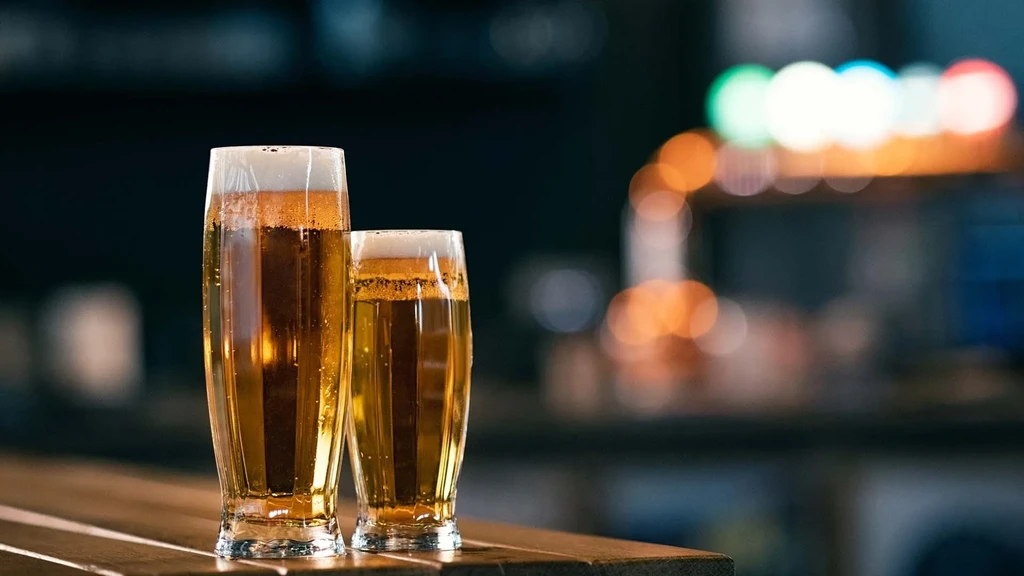 Two glasses of golden beer on a bar with colorful blurry background lights.