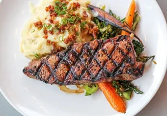 Grilled steak, mashed potatoes, carrots, and broccoli on a white plate.