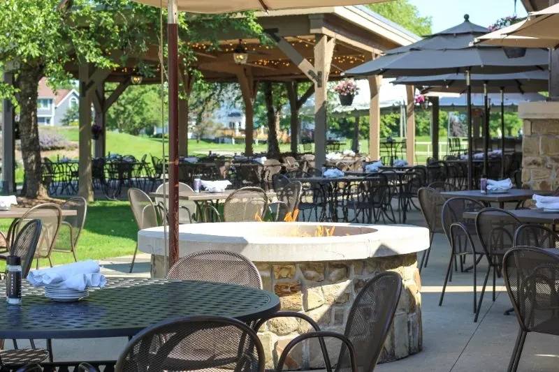 Empty outdoor dining patio with tables, active fire pit, and pergola.