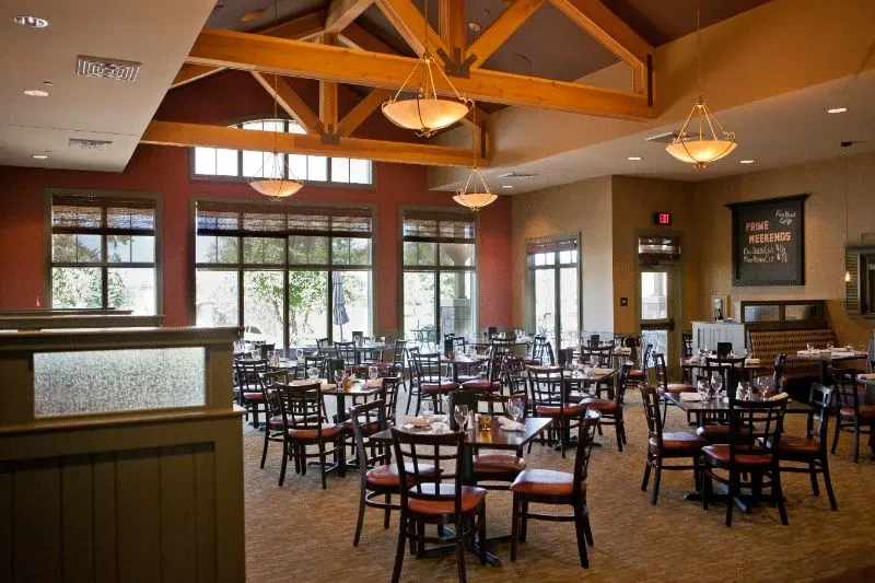 Empty restaurant dining hall with set tables, exposed beams, and menu board.