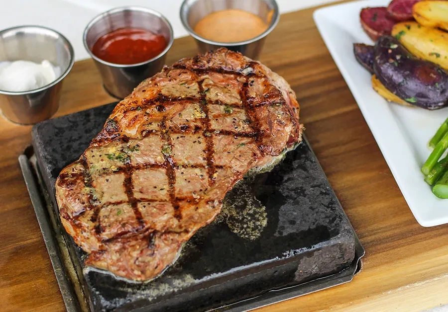Grilled steak on a sizzling hot stone with sauces and sides.