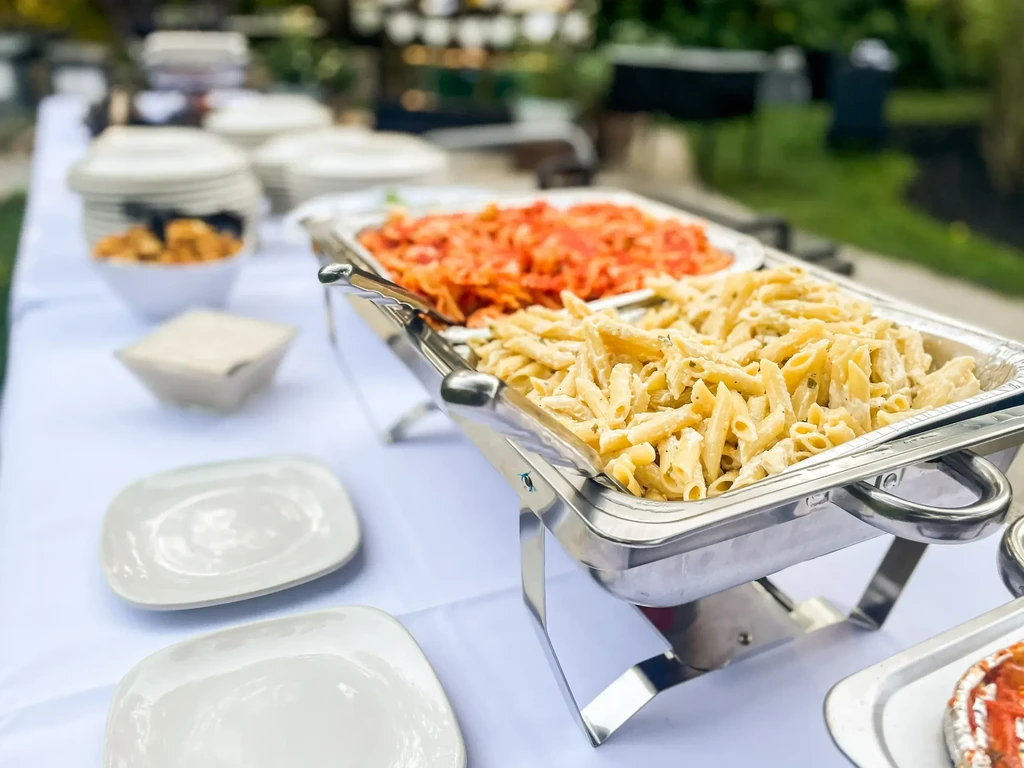 Outdoor buffet with creamy penne and red sauce pasta in chafing dishes.
