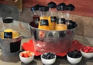 Brunch station with bottled juices, fresh berries, and metal buckets.