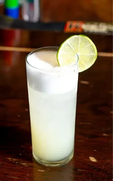 A glass of frothy pale drink with a lime wheel garnish.