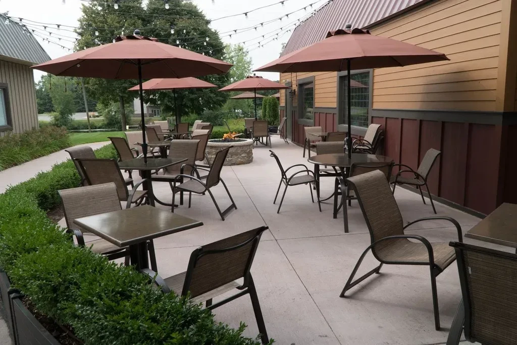 Outdoor restaurant patio with tables, umbrellas, fire pit, and string lights.