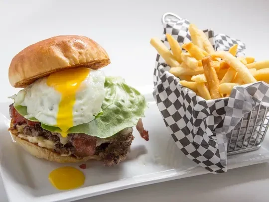 Burger with dripping egg yolk, bacon, lettuce, and french fries.