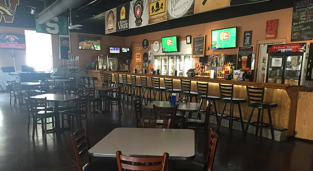 Empty sports bar interior with long bar, multiple TVs, and dining tables.