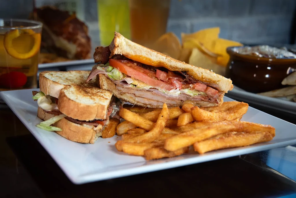 Stacked club sandwich, french fries, and cocktail on a plate.