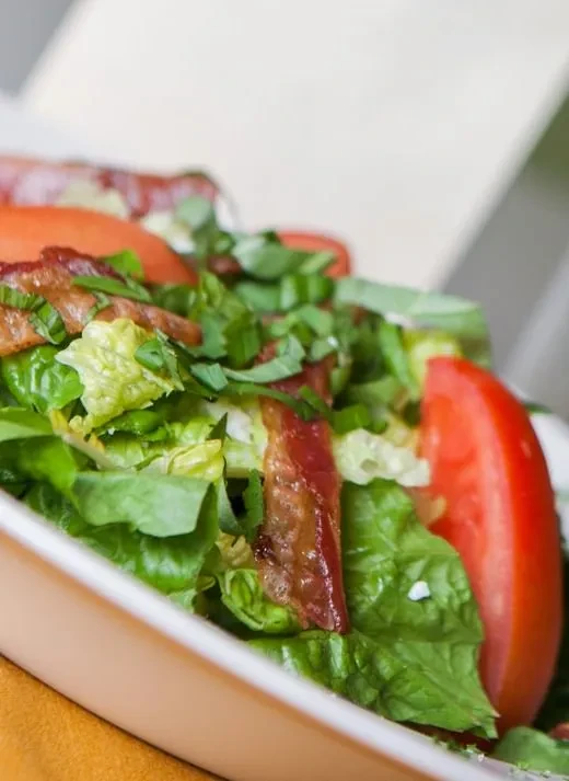 Salad with lettuce, tomato, bacon, and herbs in a white bowl.