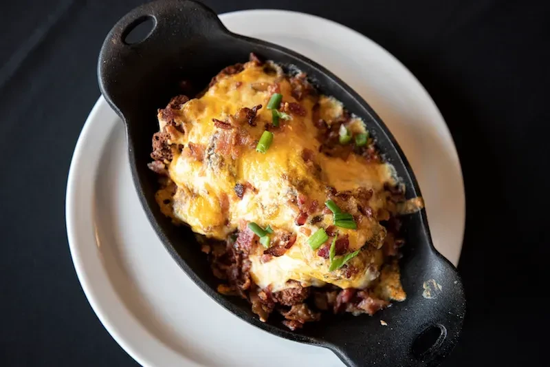 Cast-iron skillet with cheesy baked casserole, bacon, and chives.