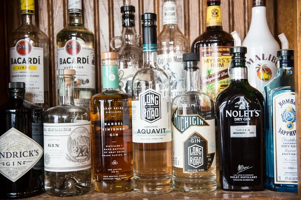 Well-stocked bar shelf of gin, rum, and aquavit bottles with pour spouts.