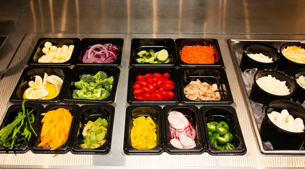 Fresh vegetables, cheeses, and toppings displayed on a salad bar.
