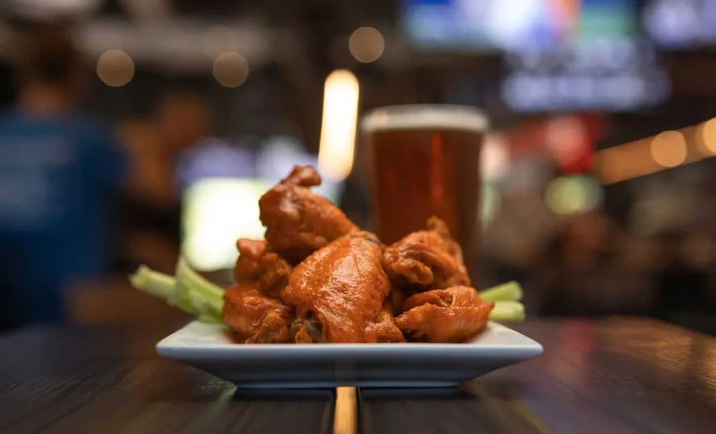 Plate of buffalo chicken wings with celery and blurred beer.