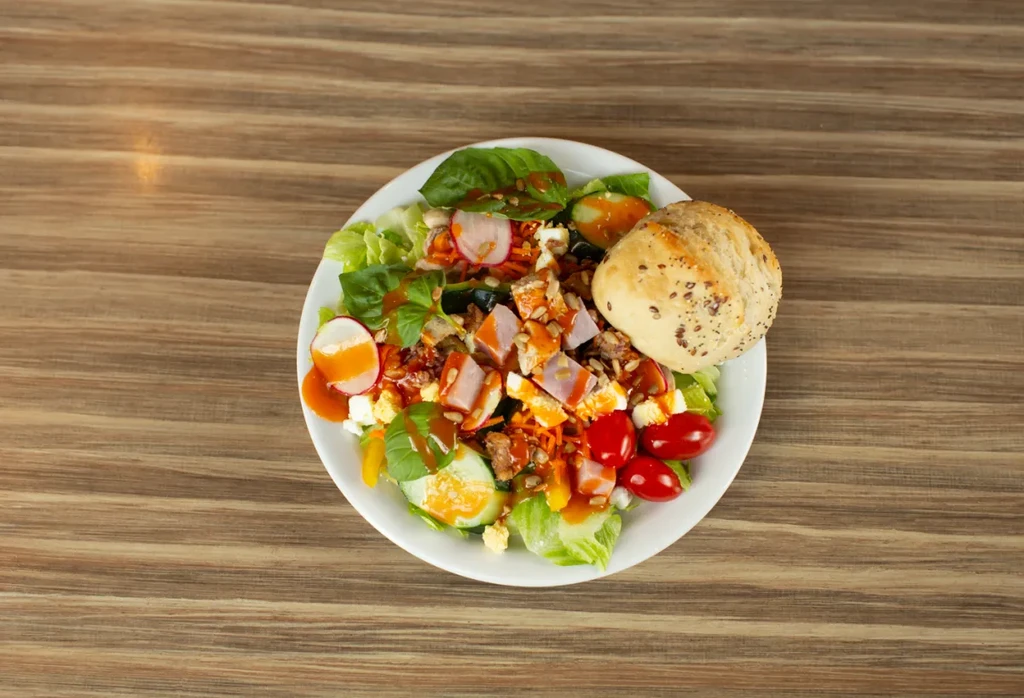 Overhead view: Vibrant salad with ham, vegetables, cheese, dressing, and bread.